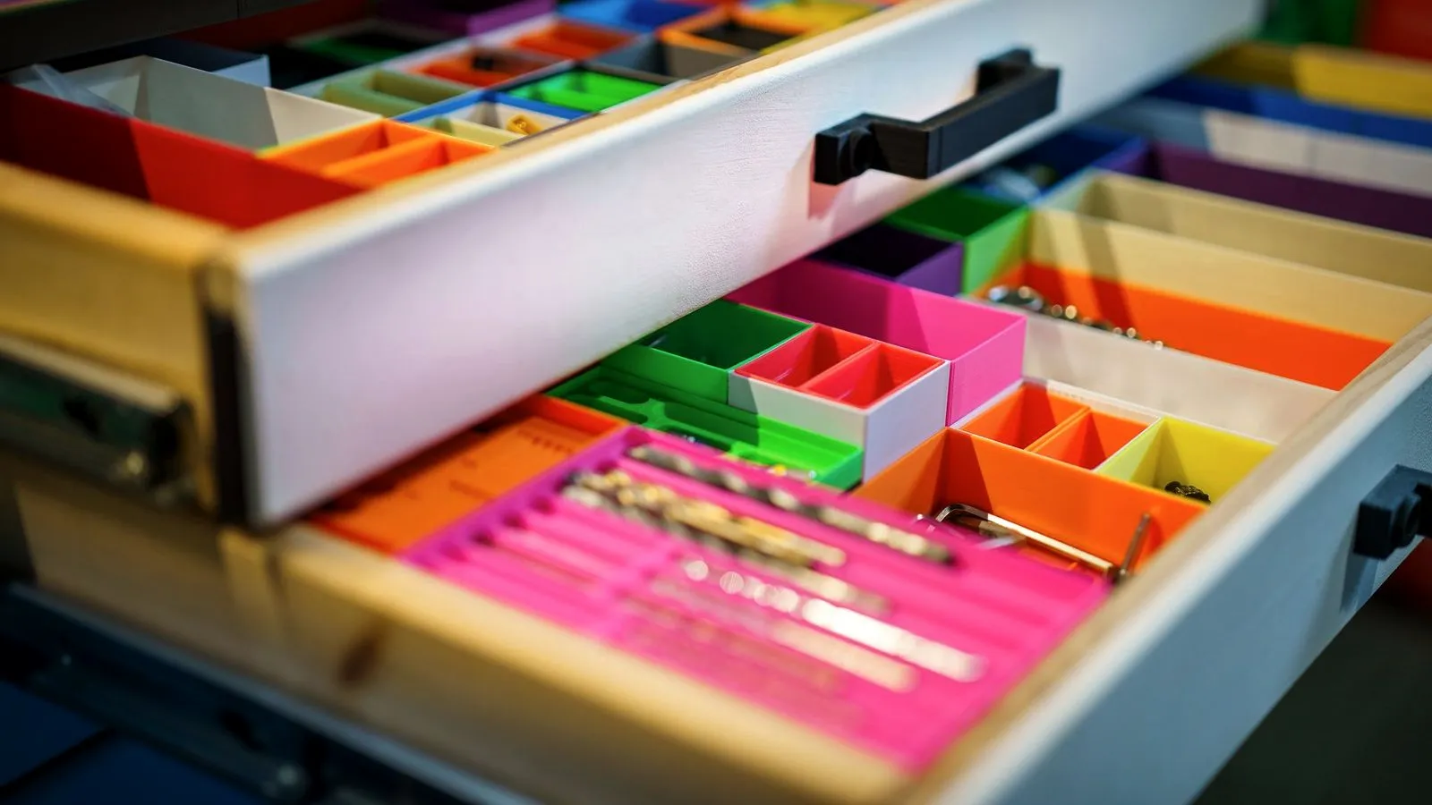 Open workshop drawer divided into brightly colored 3D printed organizer bins, one holding drill bits