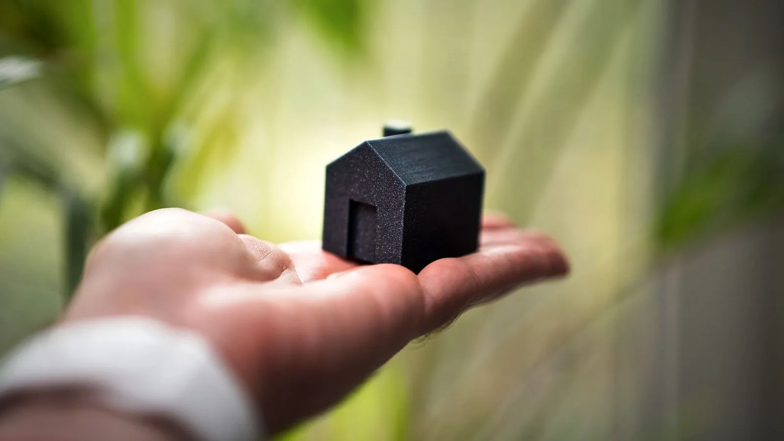 A hand holding a small black 3D printed house model