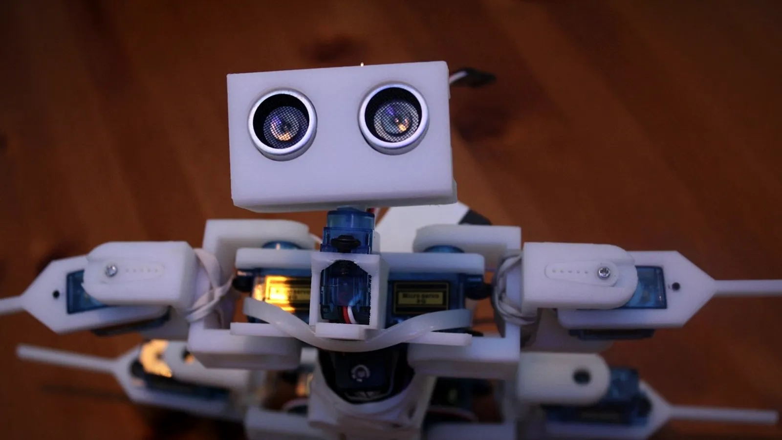 Small white 3D printed robot built with servos and a distance sensor, on a wooden floor