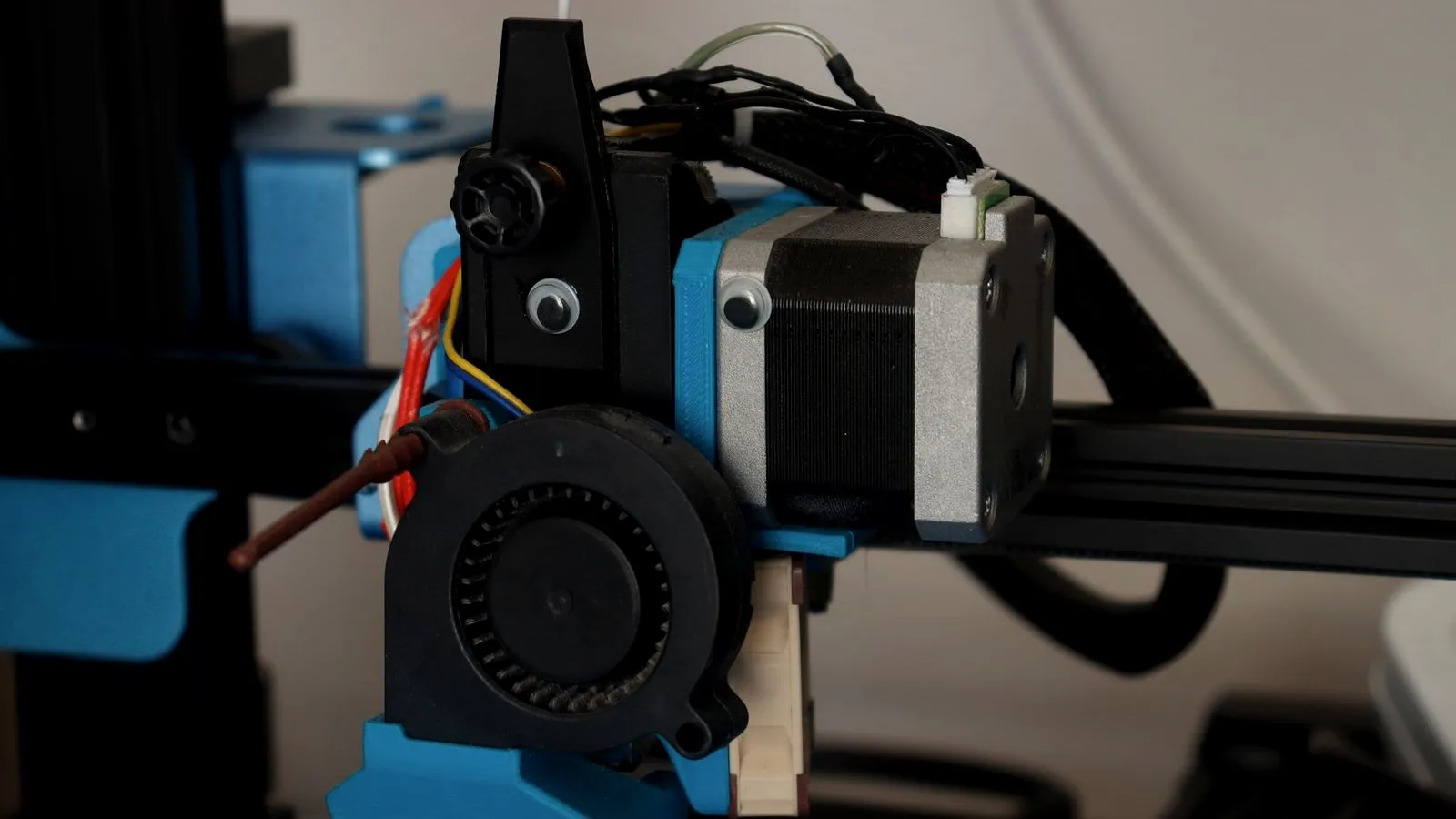 Close-up of a direct drive 3D printer extruder with its stepper motor, cooling fan and wiring mounted on the X-axis gantry