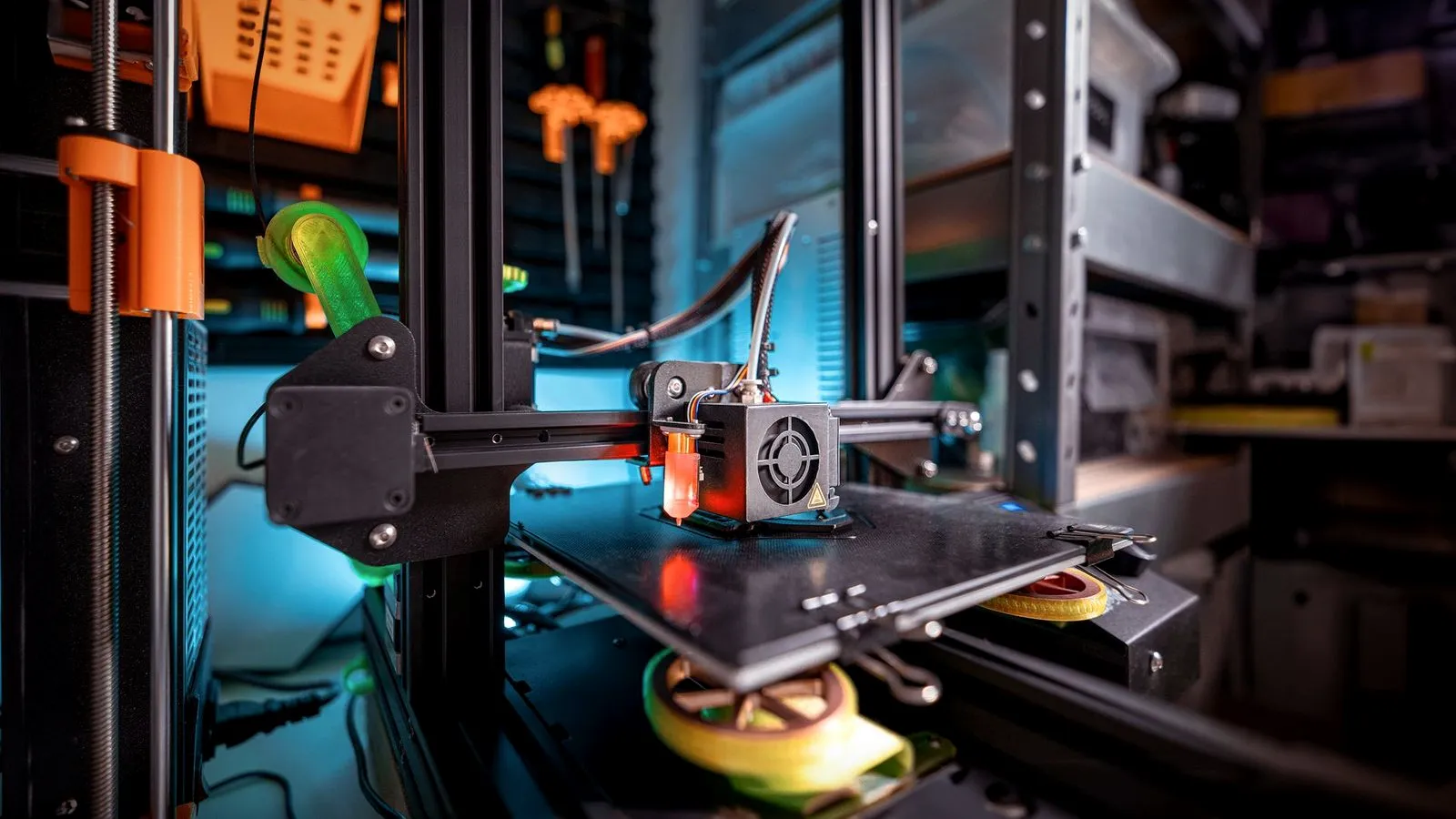 Open-frame 3D printer on a workshop shelf, with printed parts and tools behind it