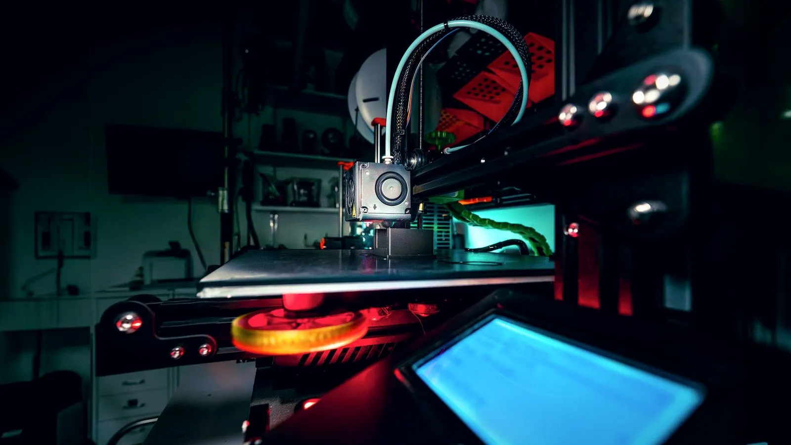 Open-frame 3D printer printing a dark part in a dimly lit workshop, its display glowing in the foreground