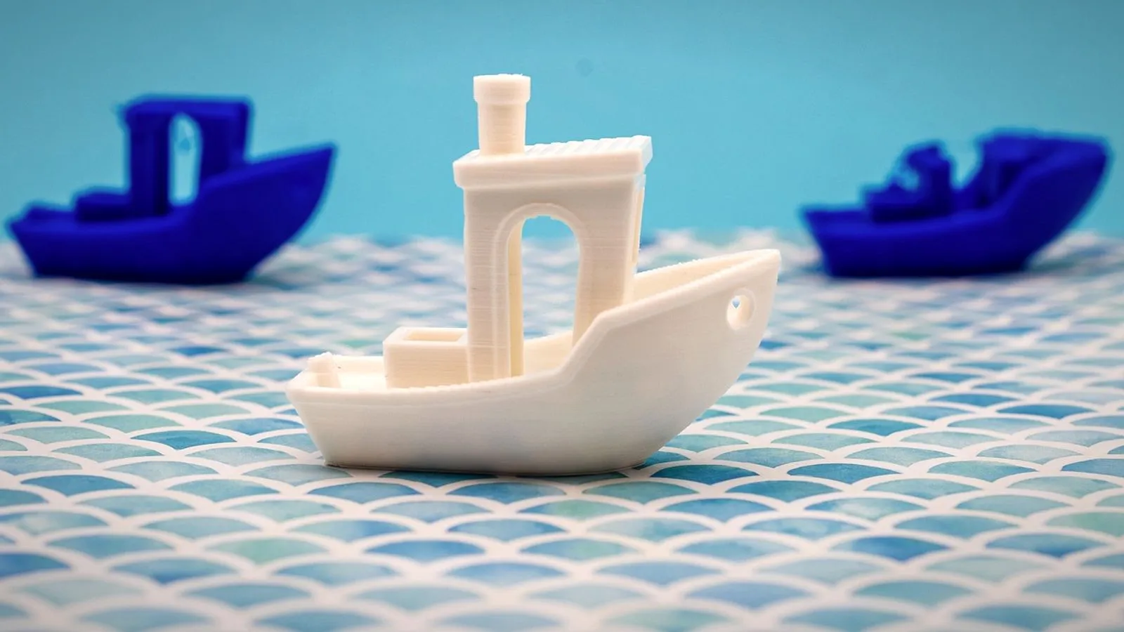 Three 3DBenchy test boats, one white and two blue, on a tiled surface