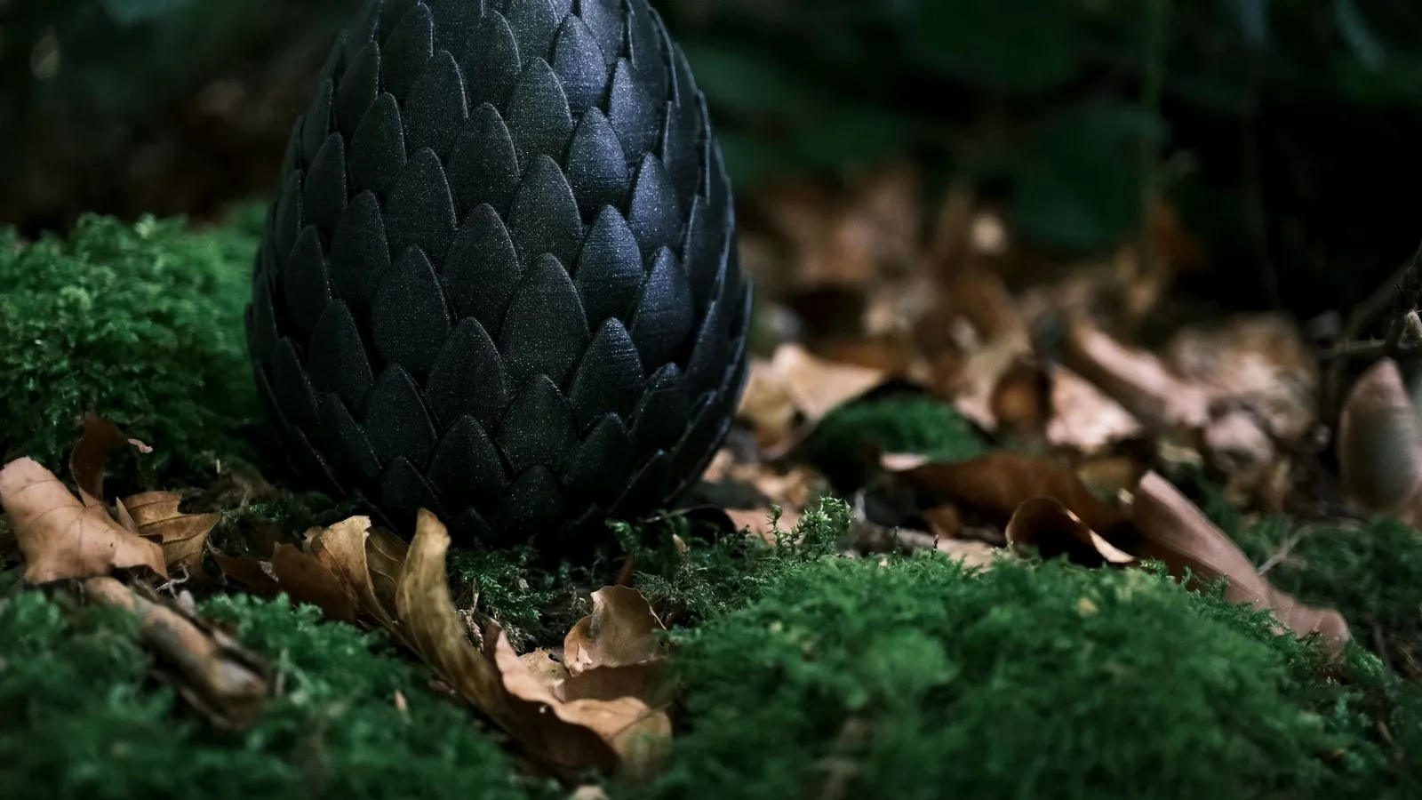 Black dragon egg sculpture with overlapping scales resting on moss
