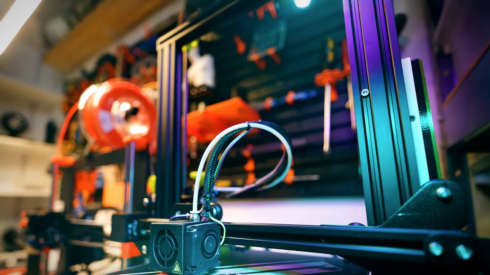 A white filament tube arching from the printer frame down to the print head in a workshop