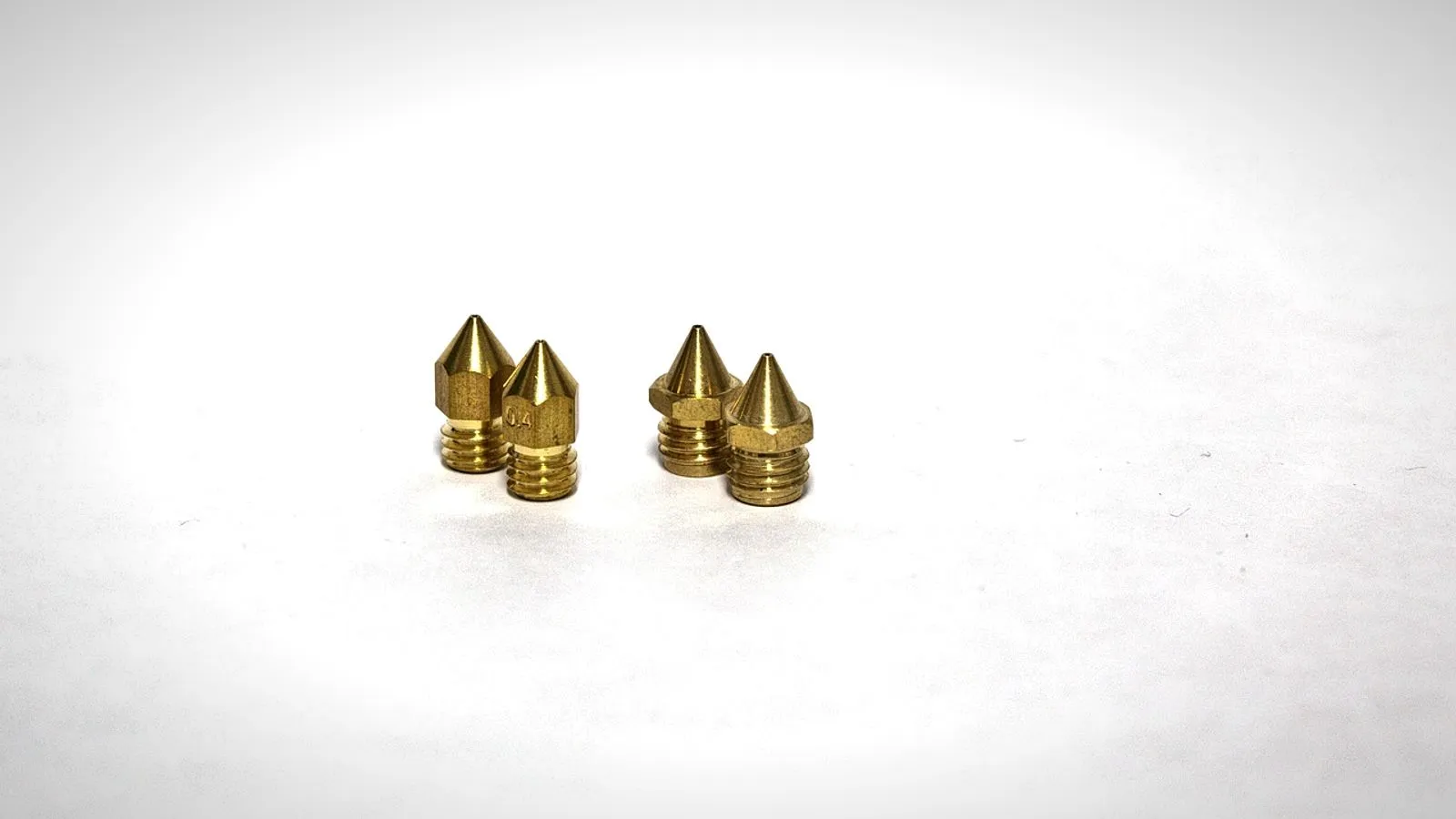 Four brass 3D printer nozzles on a white background