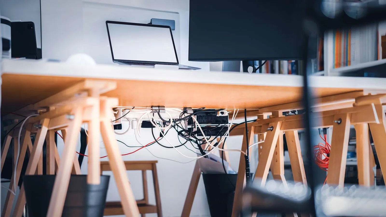 Cables and power strips clipped under a desk on wooden trestle legs