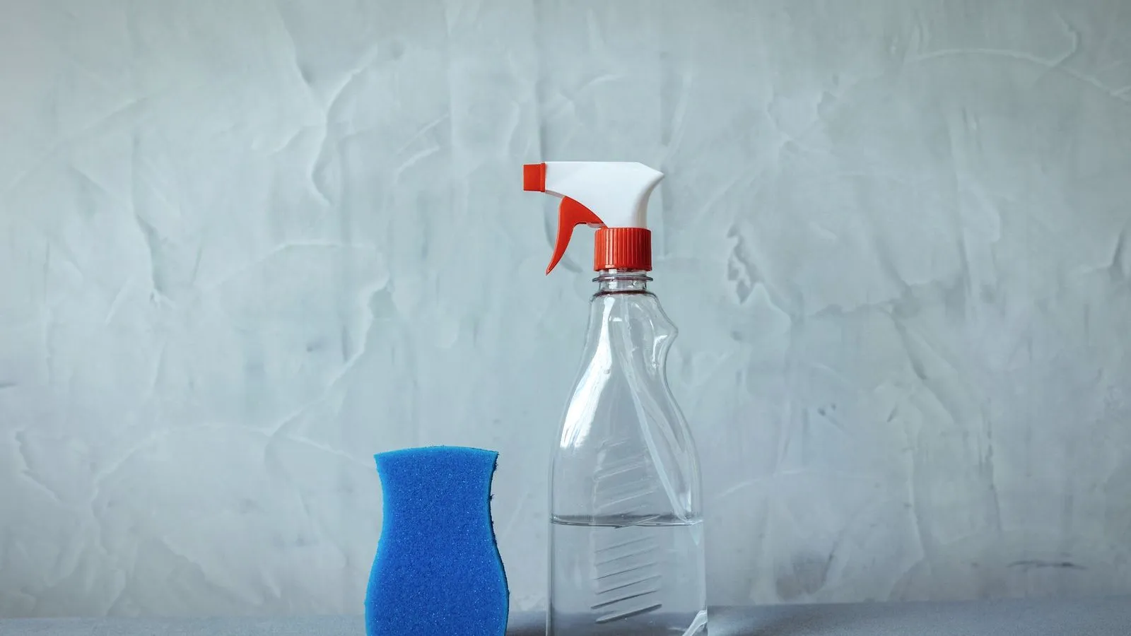 Clear spray bottle and a blue sponge on a gray surface