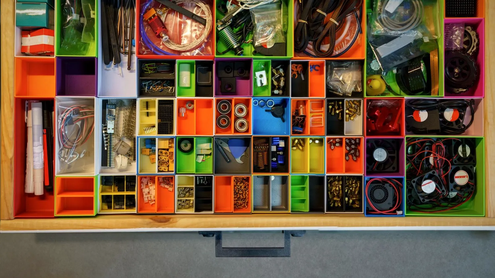 Top view of a drawer filled with colorful 3D printed bins holding fans, bearings, cables and small printer parts