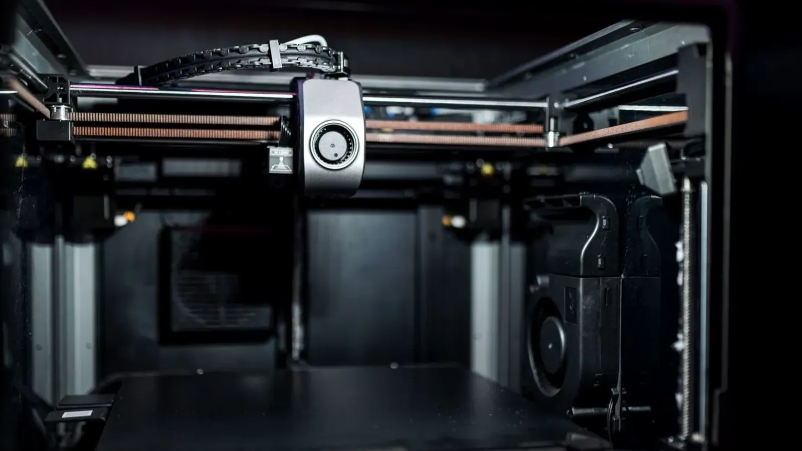Inside an enclosed 3D printer with the print head on its gantry above an empty build plate