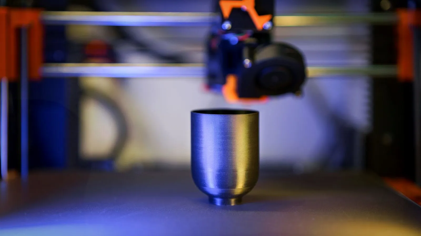 Gray cup printed on a filament 3D printer, with the print head just above it