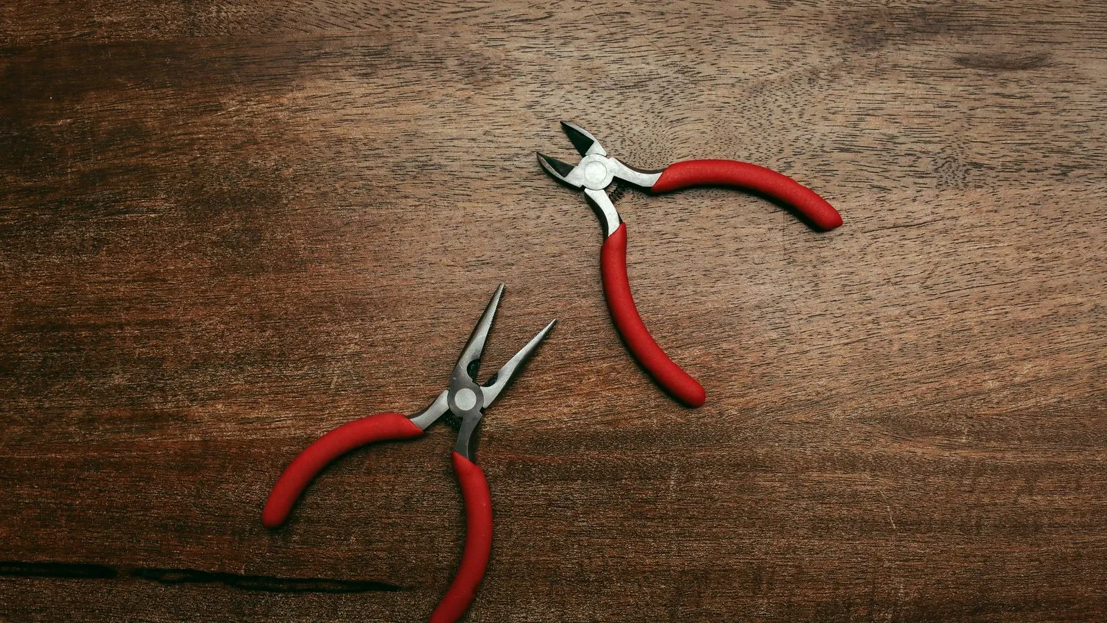 Small flush cutters and needle-nose pliers with red handles on a wooden bench