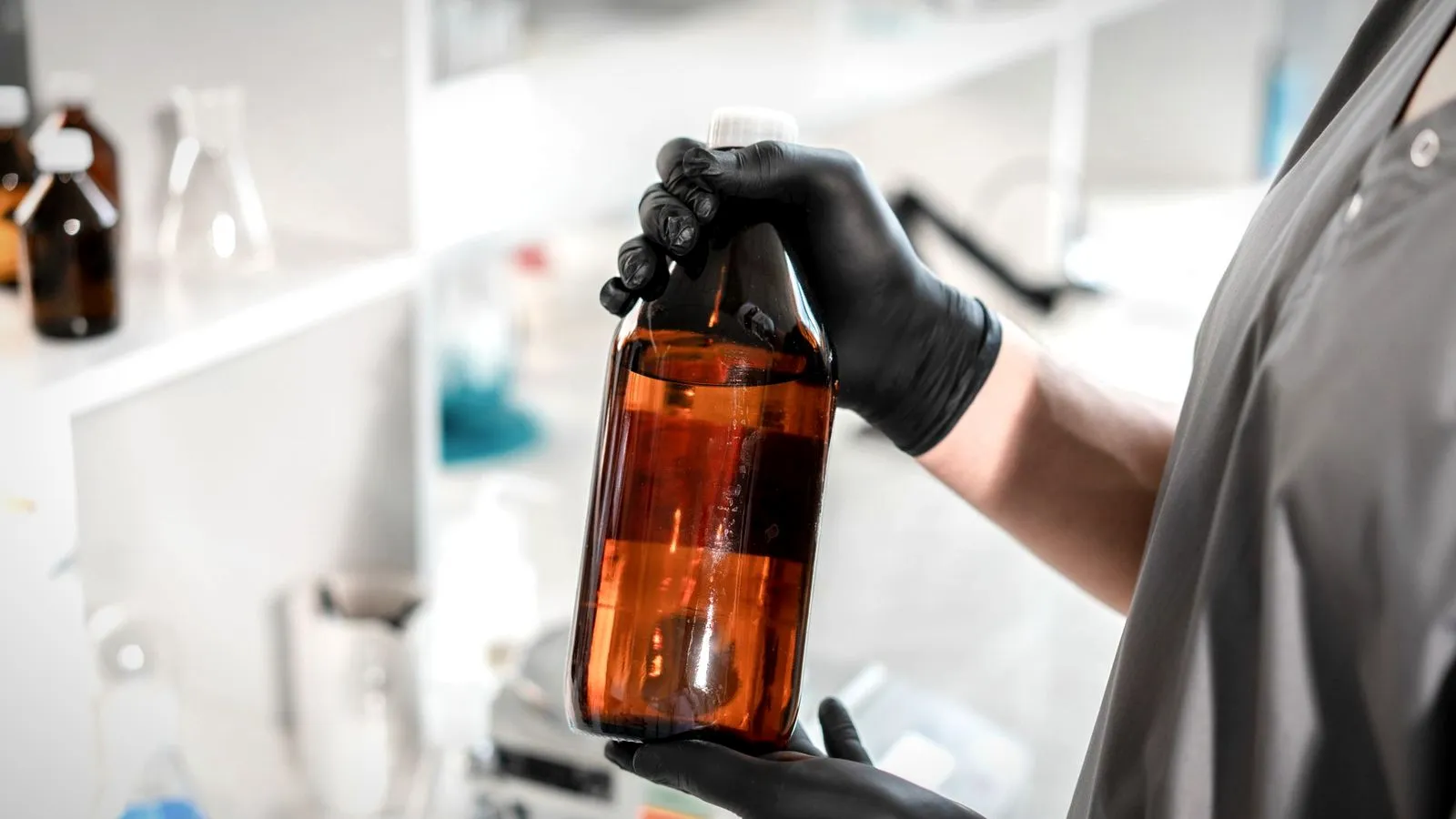 Gloved hands holding an amber, light-blocking bottle on a lab bench