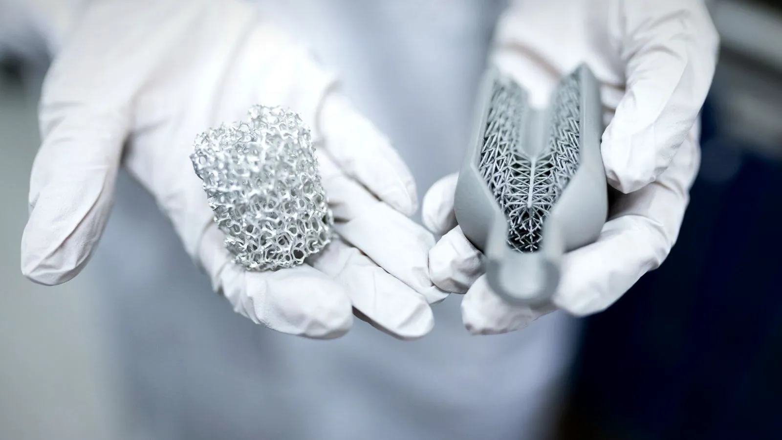 Gloved hands holding two 3D printed lattice parts in a lab