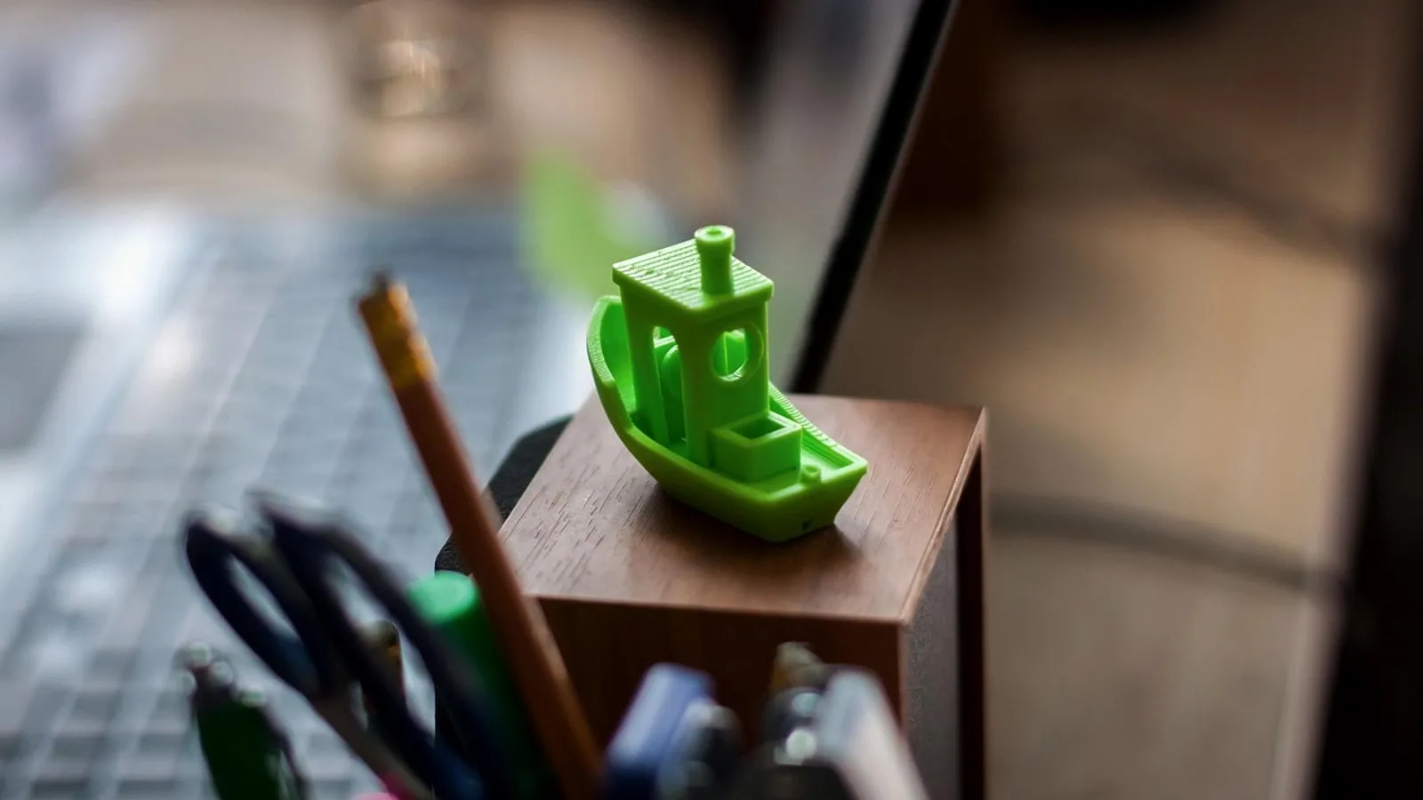 Green 3DBenchy test boat on a desk next to a pen cup and keyboard