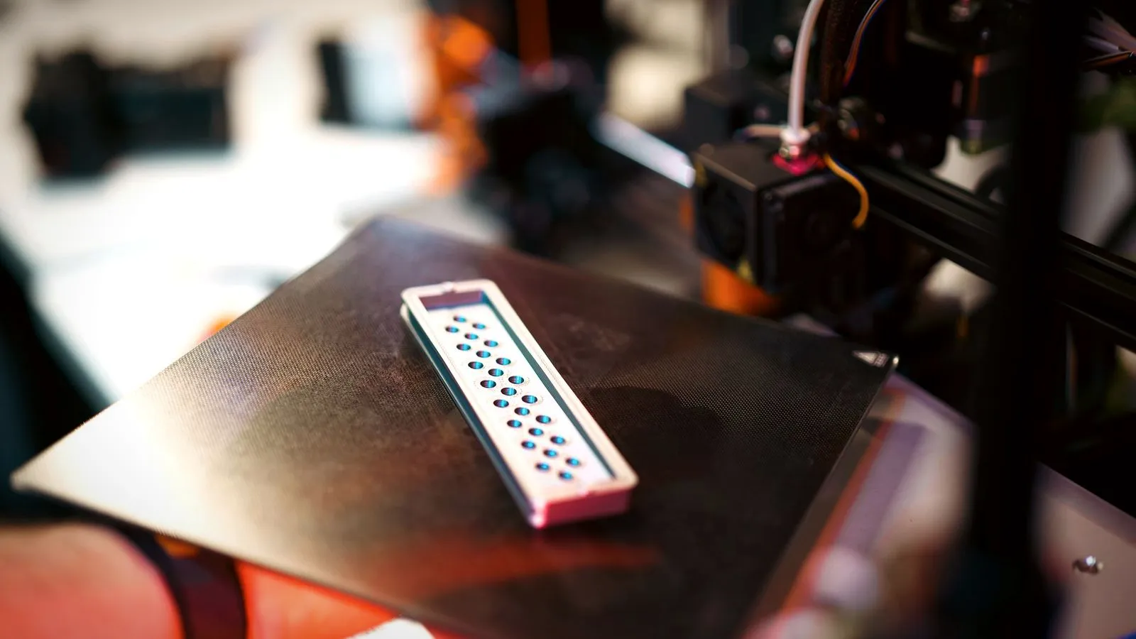Hand holding a flexible steel build plate with a freshly printed part on it
