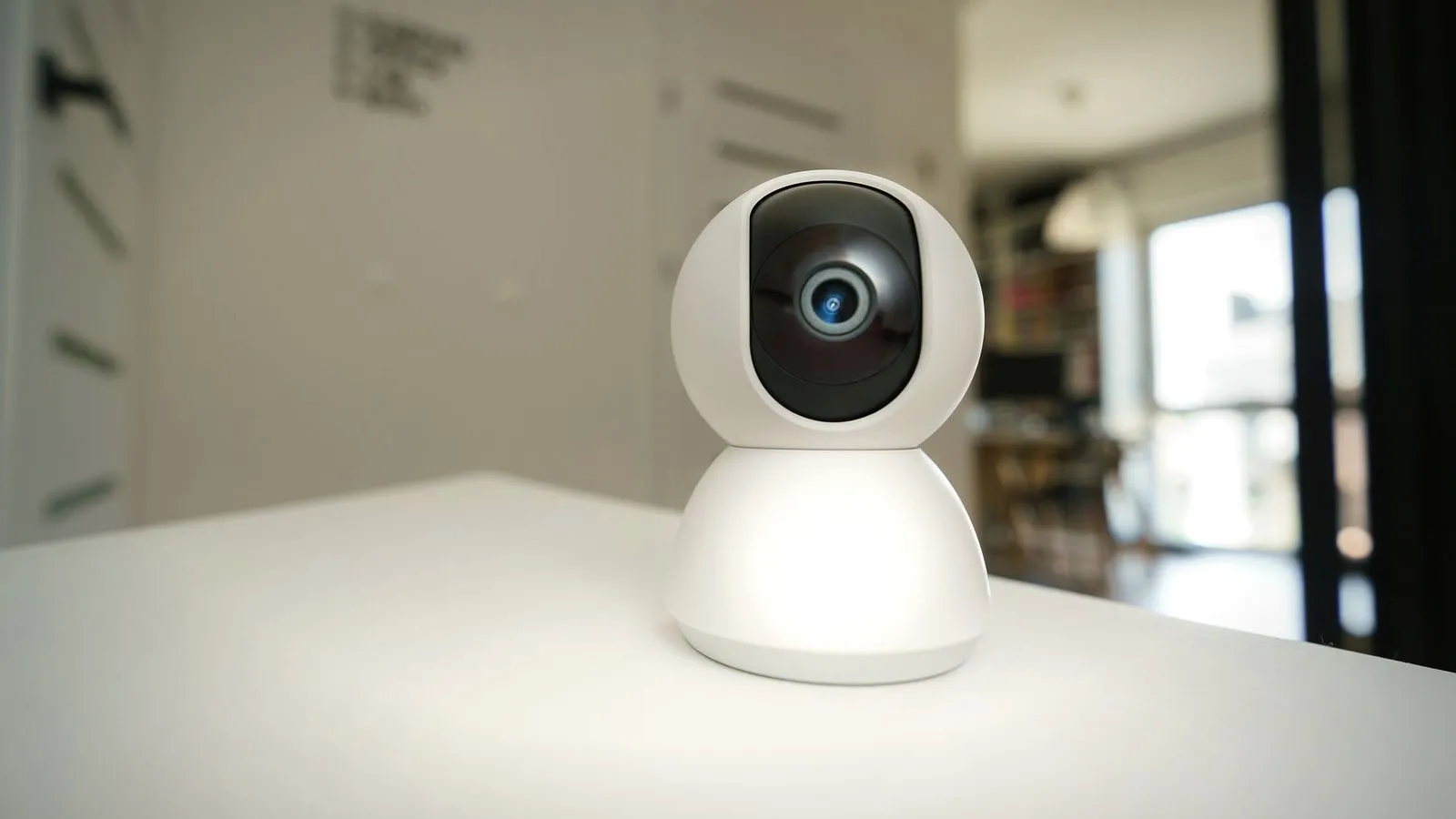 White pan-and-tilt indoor Wi-Fi camera standing on a white desk in a room