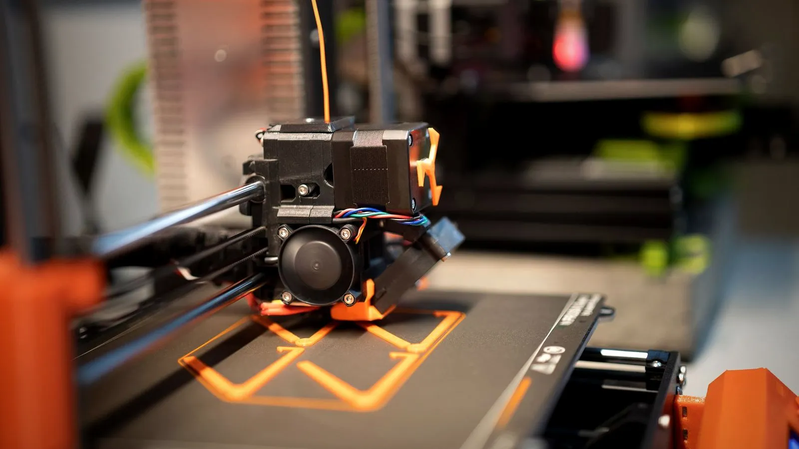 3D printer print head laying down thin orange first-layer lines on a dark build plate
