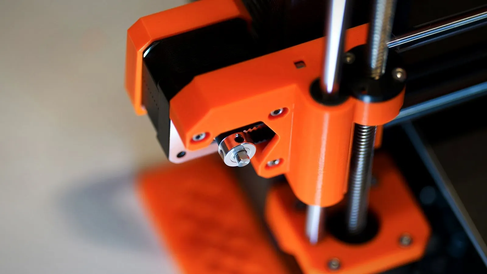 Orange 3D printed parts holding a stepper motor, smooth rod and lead screw on a printer frame, close up