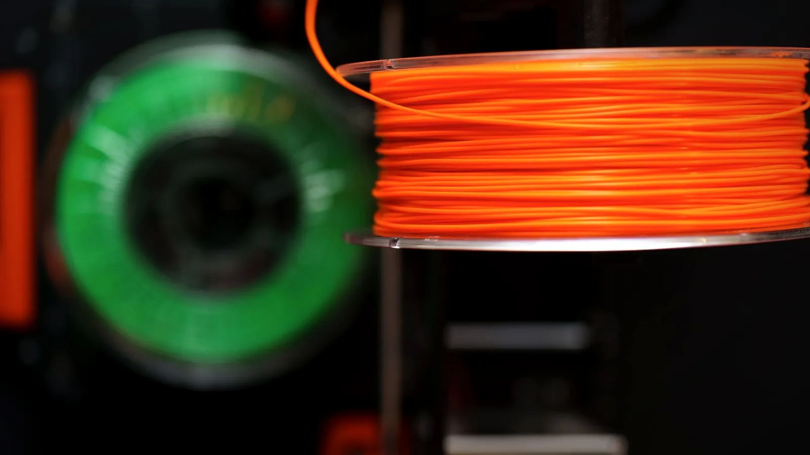 Orange filament spool on a printer's spool holder with a green spool behind it