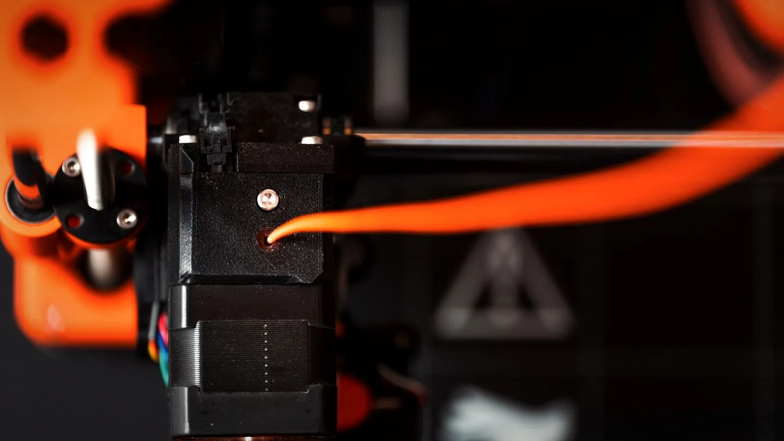 Orange filament feeding into a black extruder housing mounted on a stepper motor