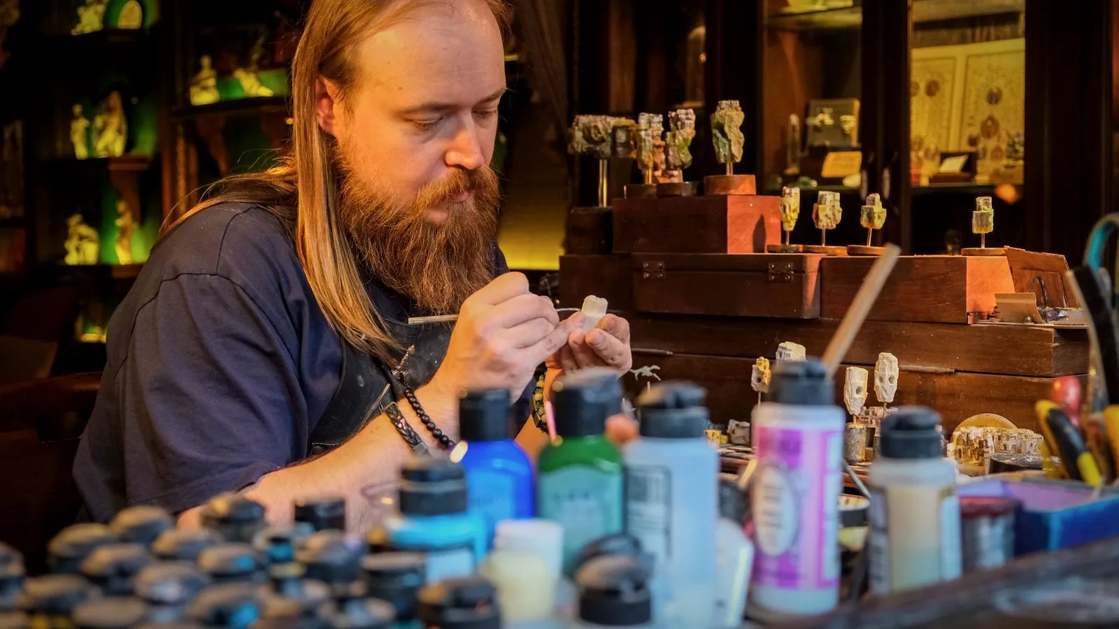 Hobbyist painting a small primed figure with a fine brush, with dropper bottles of hobby paint in the foreground