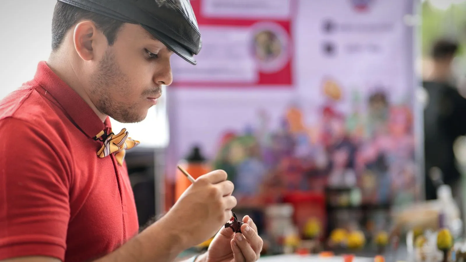 Man painting a small figurine with a fine brush at a hobby table