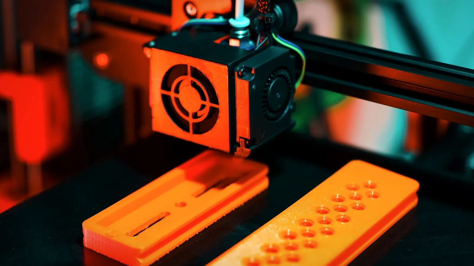 3D printer hotend printing two orange parts on the build plate