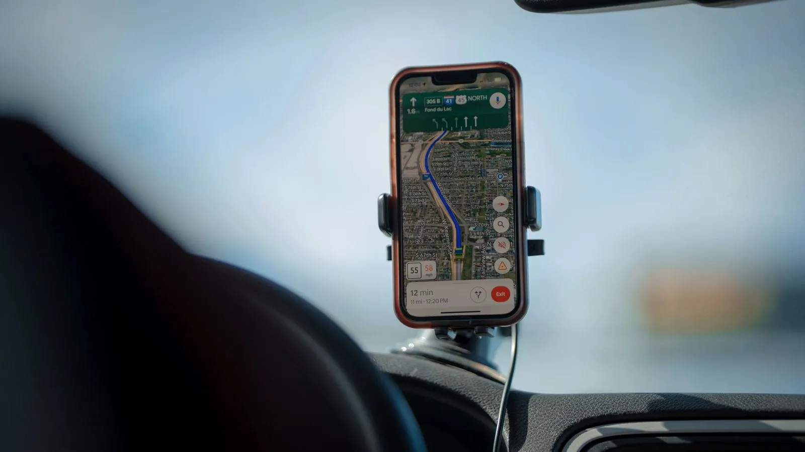 Smartphone showing a navigation map in a mount on a car windshield, seen from the driver's seat