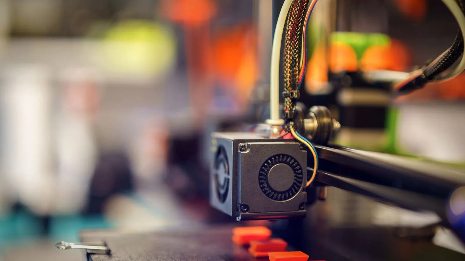 3D printer hotend above small red printed parts on the build plate