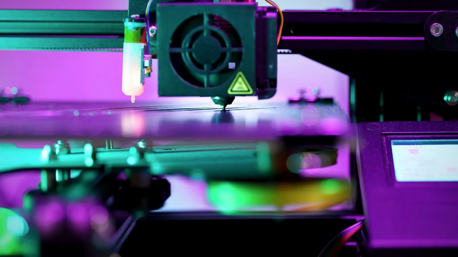 Print head with the hotend fan behind a grille, a bed probe beside it and the nozzle just above the bed, lit in magenta and green
