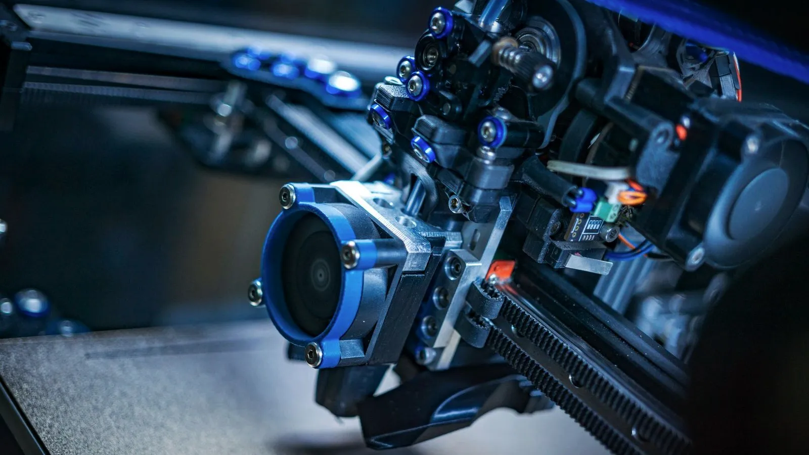 3D printer print head with a blue cooling duct positioned over a textured build plate