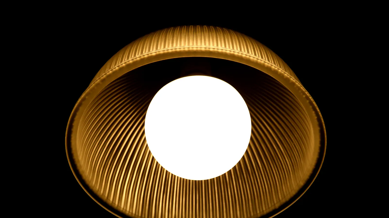 A ribbed, translucent lamp shade glowing around a round bulb against a dark background