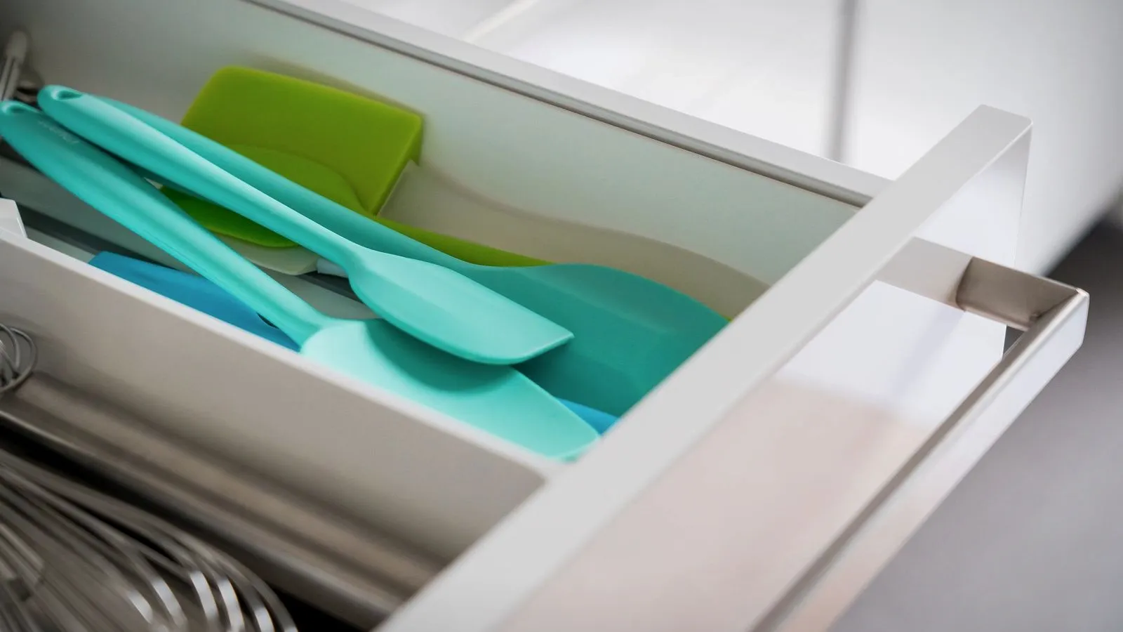 Teal and green silicone spatulas in an open white drawer