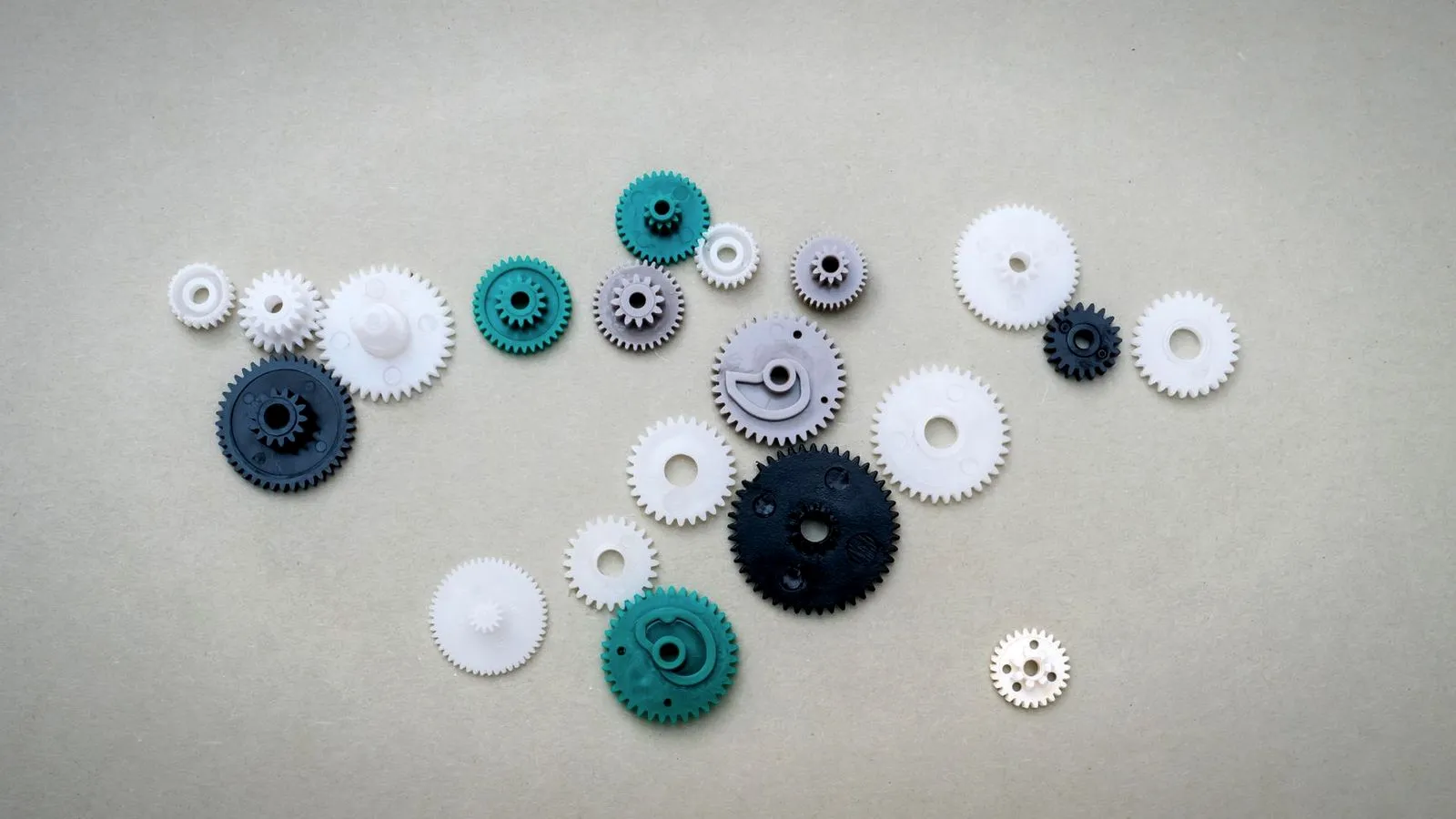Assorted small white, gray, teal and black plastic gears on a gray surface
