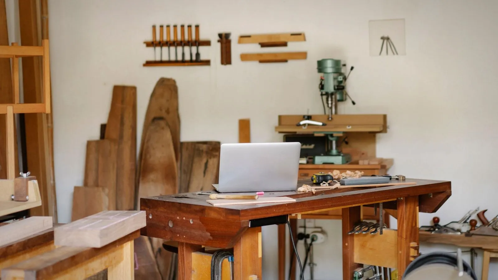 Solid wooden workbench with a laptop and a small drill press in a bright workshop