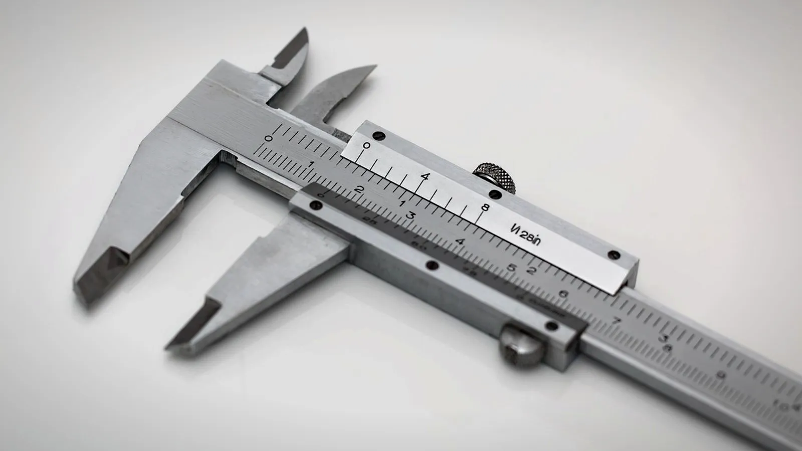 Steel vernier caliper with its jaws slightly open, lying on a white surface