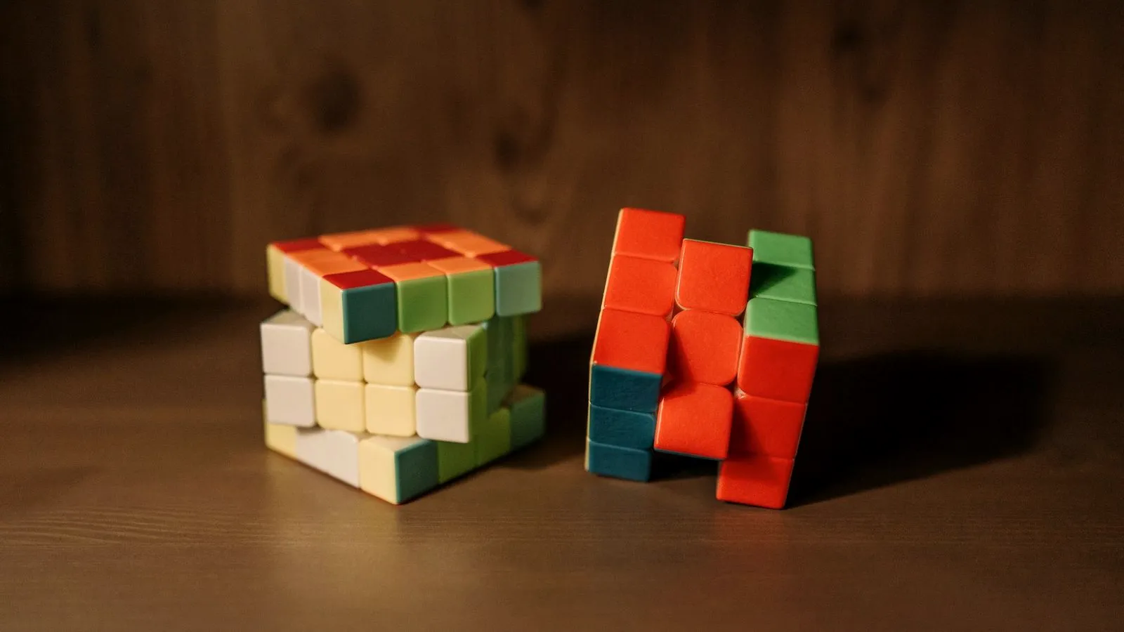 Two partly solved puzzle cubes on a wooden surface