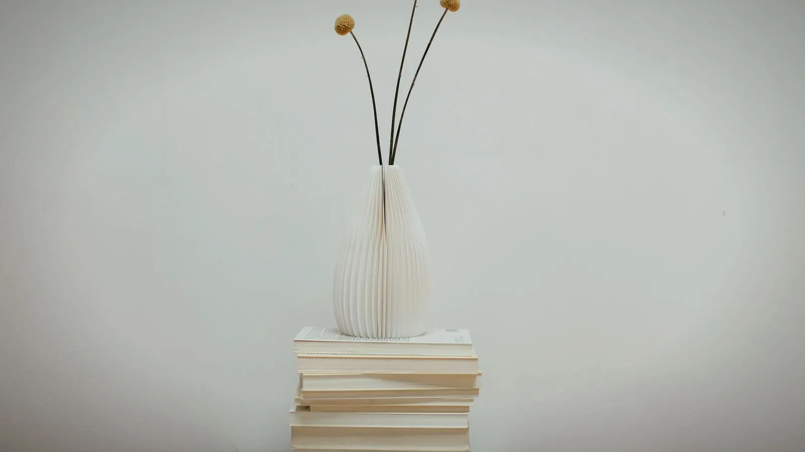 White ribbed vase with dried flowers displayed on a stack of books